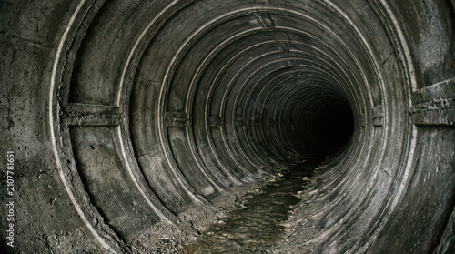 A dark concrete tunnel with ribbed walls and a small stream of water at the bottom, leading into a dark abyss, suggesting a sense of mystery and depth, creating a dramatic and intriguing visual