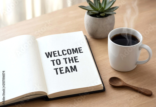 Open notebook with welcome to the team message beside coffee and plant on desk setup