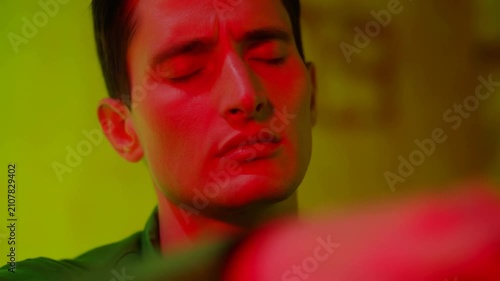 Male individual with closed eyes and focused expression interacts with a colorful illuminated surface, showcasing gradual hand movement in a dimly lit environment