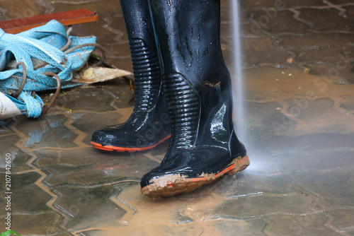 Bilde på lerret Black work boots being sprayed clean with high pressure stream on wet muddy pave