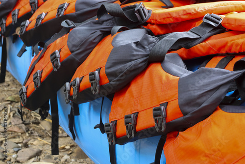 Bright orange life jacket arranged on blue kayak with black buckles and straps, outdoor gear ready for water adventure and safety on rocky shore
