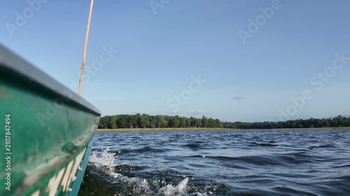 Low angle POV shot of green wooden boat hull sailing through water on sunny lake