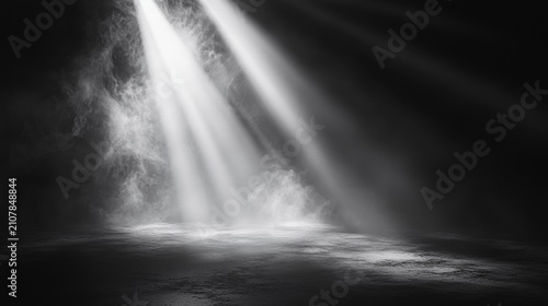 A dramatic black and white image showing beams of light piercing through darkness onto a textured floor with mist or smoke in the air.