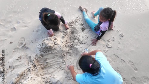 Happy mother and daughters building sandcastle together on tropical beach during summer vacation