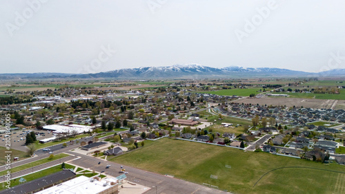 Bild auf Leinwand Aerial view of an open green field bordering a growing residential subdivision near mountains