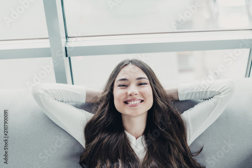 Foto Smiling young woman relaxing on a couch by a bright window, casual lifestyle por