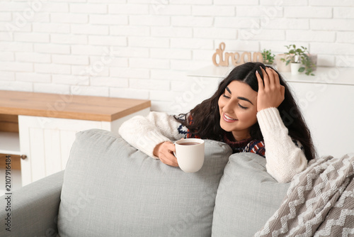 Beautiful young woman with cup of hot tea in living room