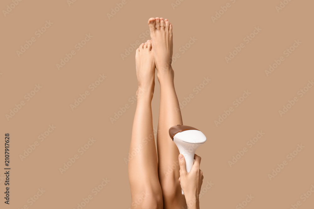 Naklejka premium Legs of young woman with modern photoepilator on brown background
