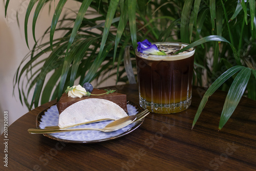 Quadro su tela Exquisite chocolate cake on patterned plate with golden cutlery, paired with a refreshing, layered iced drink garnished with blue butterfly pea flower in a cozy cafe