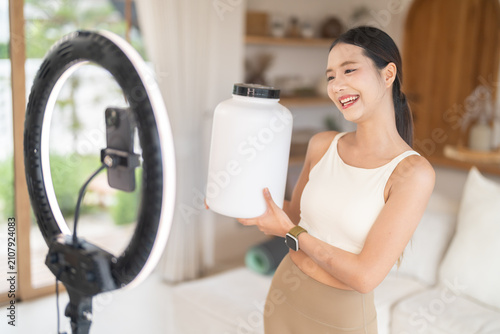 Fitness asian influencer creating social media content with smartphone and ring light, Content creator live streaming health supplement product mockup at home, Vlogger, active lifestyle and wellness