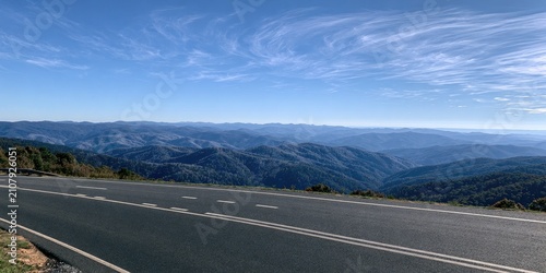 Paved road overlooks vast, blue mountain ranges under a vast sky