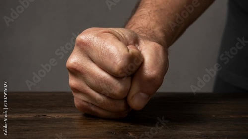 Close up of a clenched fist on wooden table showing anger and determination