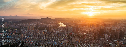 Fotografie A high-angle aerial panorama captures a sprawling urban cityscape at sunset, backed by distant mountains under a golden sky