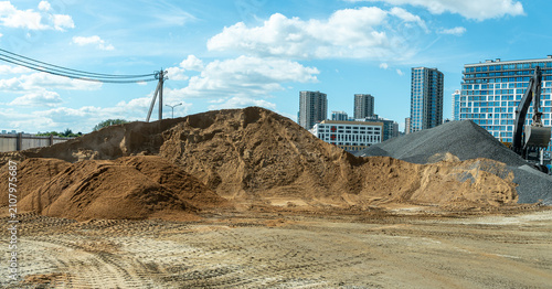 Construction site with large heaps of sand and gravel on modern cityscape background heavy machinery excavator working on urban development project area
