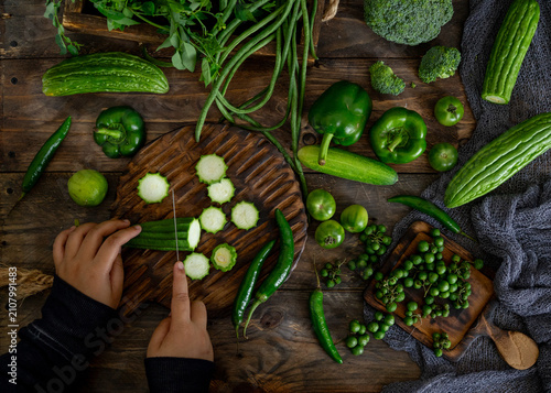 Fotografie Top view of hands slicing fresh green vegetables on a wooden cutting board with