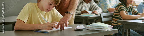 Фотография Header of teen students studying and writing in classroom while teacher guiding schoolwork, supporting learning and academic progress