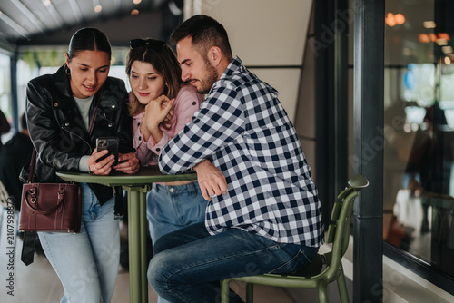 Obraz na płótnie Three young friends gathered around a smartphone, smiling and focused on the screen