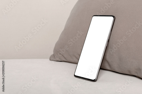 Smartphone leaning against a pillow on a sofa. Blank screen mockup in a minimalist home interior. Copy space for app design and device advertising..