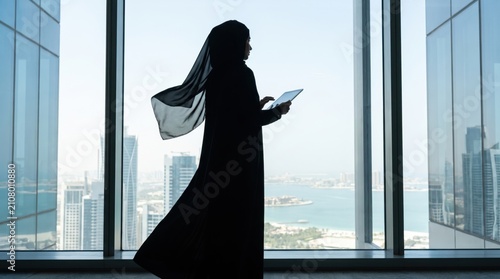 Silhouette of a Muslim Woman in Hijab Using a Tablet in a Modern Office.