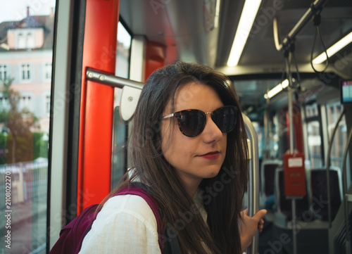 Fotografía Young woman with sunglasses glancing over her shoulder on a tram