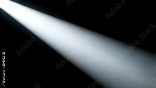 Bright spotlight beam shining through darkness with atmospheric smoke and dramatic lighting effect.