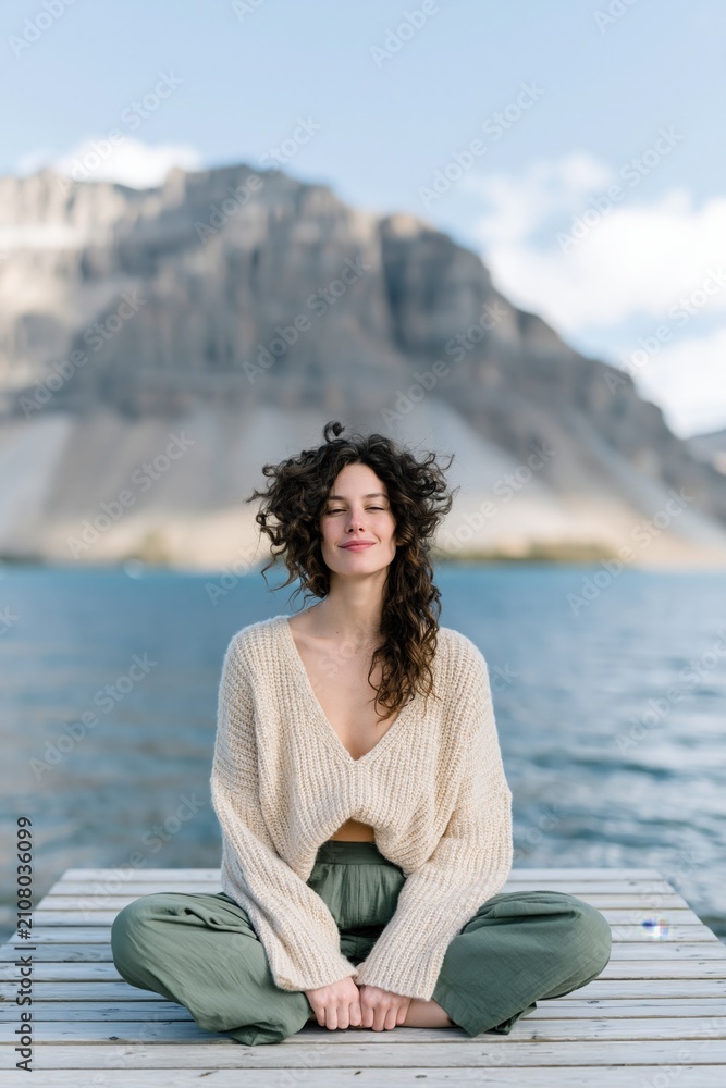 Fototapeta premium Young woman meditating on a dock by a mountain lake for serene wellness background and banner design