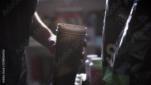 Man pouring scoop of weight gainer powder into fitness shaker bottle close up