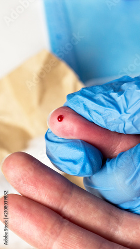 Obraz na plátne Close-up finger of person wearing blue medical glove shows small drop of blood o