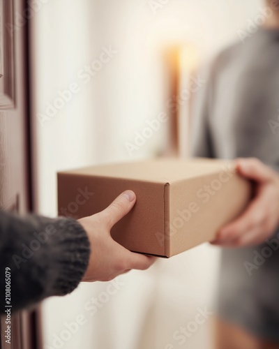 Delivery man handing brown cardboard package to customer at residential door. Online order shipping and delivery service