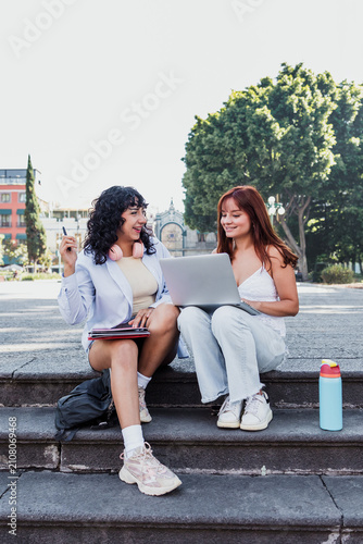 two young latin university women students using laptop sitting on bench park outdoors in Mexico Latin America, hispanic girls studying 
