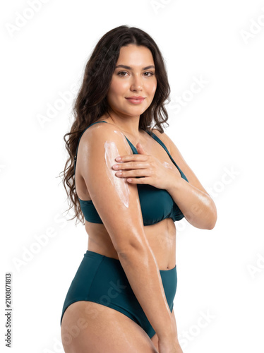 Smiling young woman in a bikini applying hydrating body lotion to her arm, demonstrating a skin care routine and beauty regimen, Isolated on a Transparent Background PNG