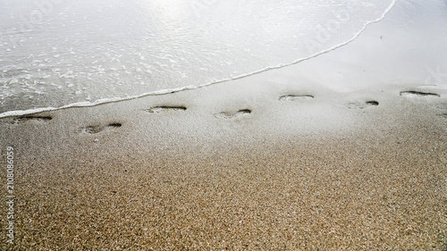 Obraz na płótnie Footprints in sand along ocean shore with receding wave