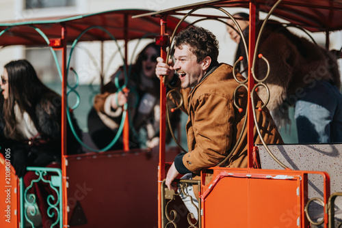 Cuadro en lienzo A group of friends ride a colorful miniature train led by a laughing young man leaning from the carriage