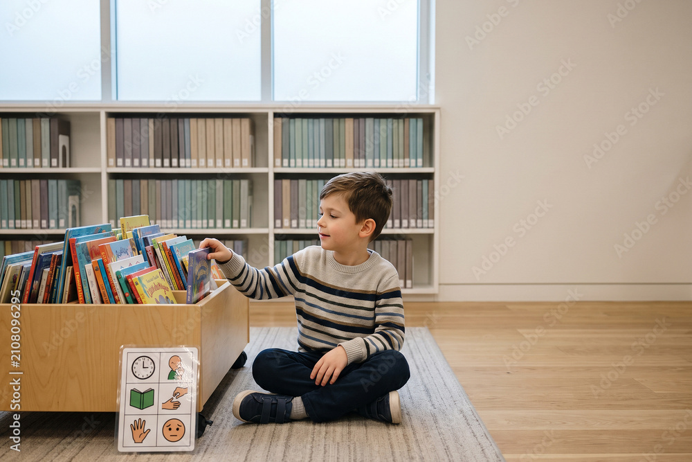Fototapeta premium Child Reading Library Books With Visual Schedule Board