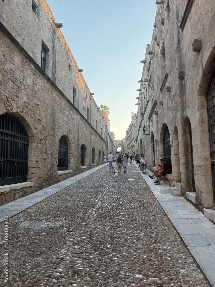 Fototapeta premium Handsome man in a burgundy linen shirt posing near the Palace of the Grand Master in Rhodes Old Town, medieval stone walls, Greek island, golden hour, elegant travel lifestyle