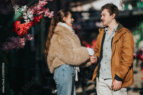 Quadro su tela A young couple of friends chat while holding hands outdoors in casual winter coats