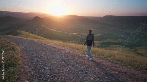 Young woman hiking along a dirt path on a hill overlooking a beautiful sea bay at sunset. Cinematic steadicam follow shot footage for active lifestyle, summer travel and freedom video.	