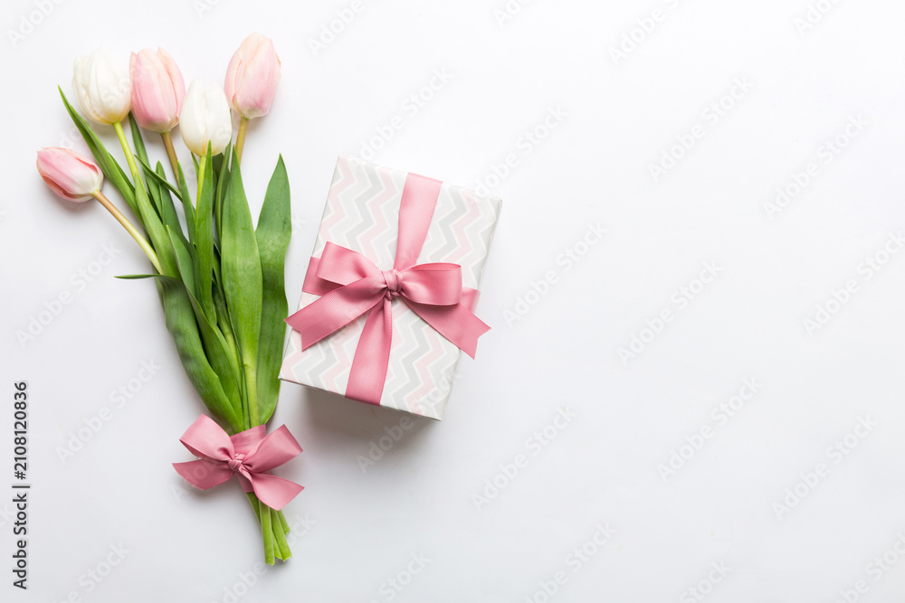 Fototapeta premium Pink tulips flowers and gift or present box on colored table background. Mothers Day, Birthday, Womens Day, celebration concept. Space for text top view