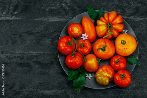Фотография Assorted red and orange homegrown heirloom tomatoes with green leaves and small