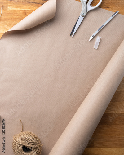 Top view of wrapped Christmas presents with kraft paper, twine and evergreen branches on a rustic wooden background with copy space.
