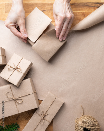Minimal Christmas flat lay featuring wrapped gift boxes, kraft paper and evergreen branches on a rustic wooden background with generous copy space.