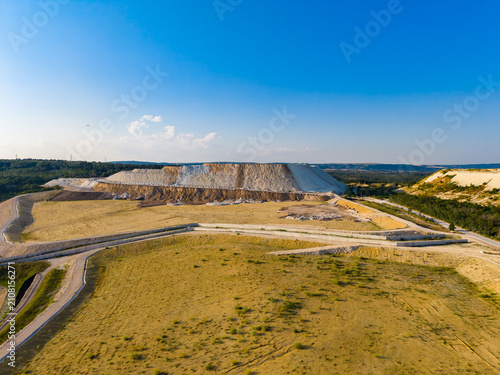 Large landfill site is seen with layers of waste and open land with dirt roads and clear blue sky in the background