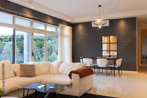 White L-shaped sectional sofa is anchoring open-plan living dining area with nested black tables