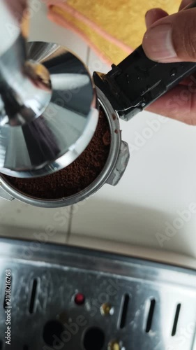 A top-down close-up view of a barista using a metal coffee tamper to press down freshly ground coffee inside a portafilter basket during the espresso preparation process