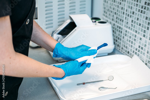 Fotografie Gloved hand uses small wrench tool to tighten attachment tip on dental handpiece over paper towel