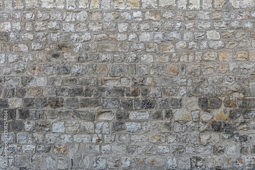 Old natural limestone wall built from irregular rectangular stone blocks with visible mortar joints. Weathered masonry texture 