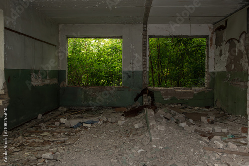 Decaying interior of abandoned building with greenery in broken windows. Dusty floor and peeling paint create a haunting, atmospheric scene