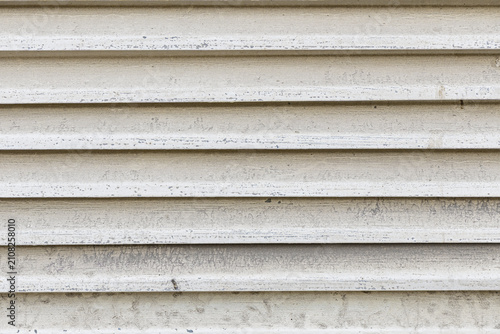 Close-up of weathered white metal roller shutter with horizontal slats. Industrial textured background showing worn painted surface with subtle dirt and aging. 