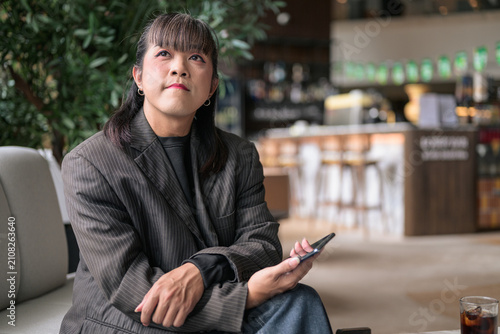 Asian Person Sitting in Cafe Lounge Gazing Off-Camera Contemplatively