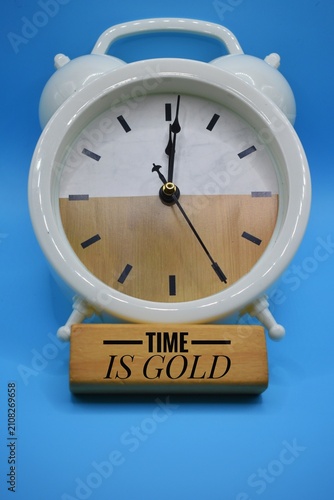 A white analog alarm clock features a two-tone face with a wooden bar displaying the phrase 